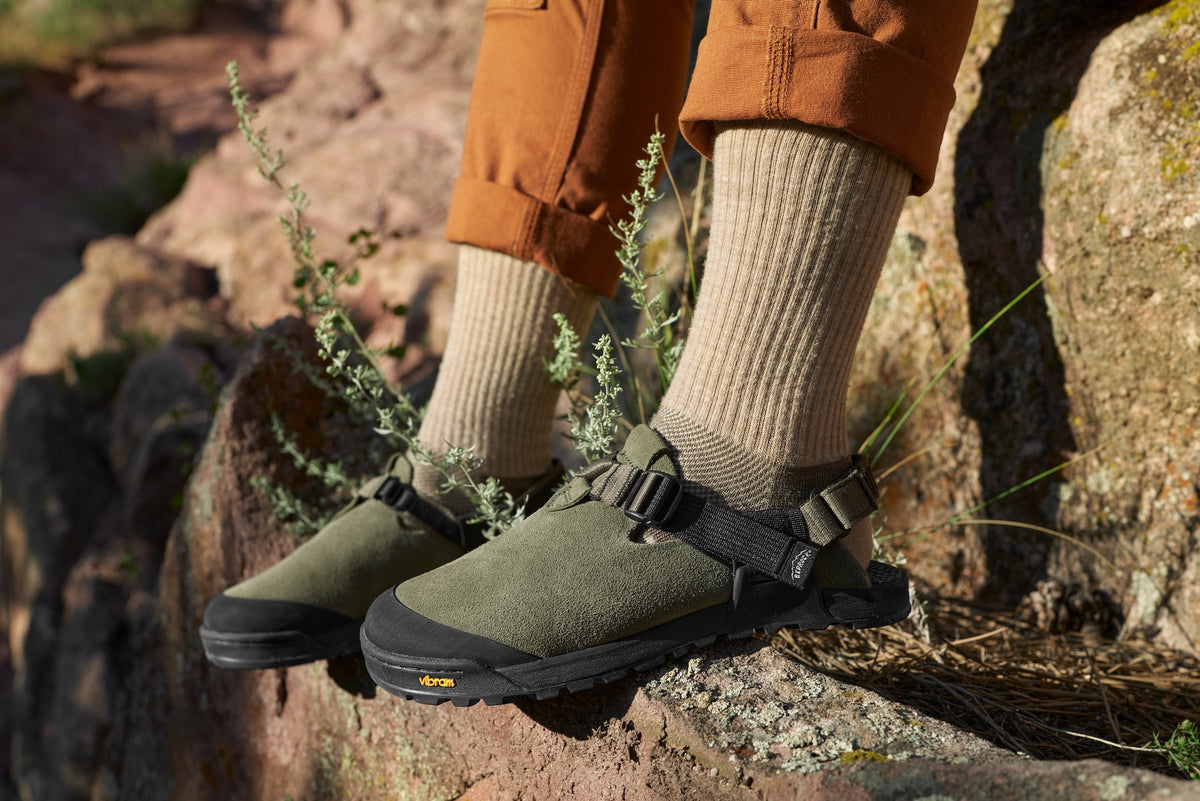 A close up of person wearing a pair of Lateral view of sagebrush green leather suede mountain clogs outside