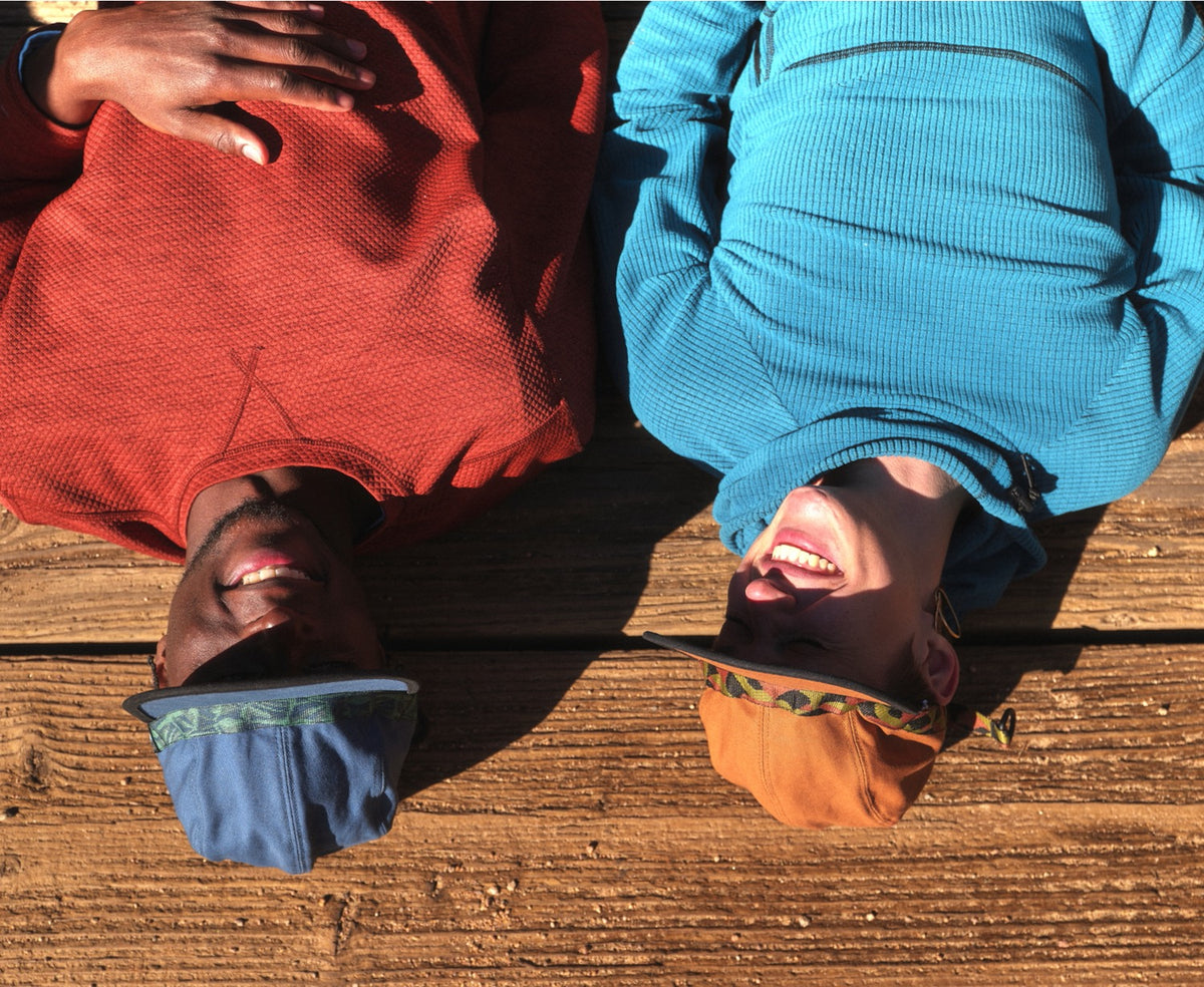 Two people laying on a wooden bridge wearing blue and brown colored organic cotton canvas fabric hat webbing by KAVU and Bedrock.