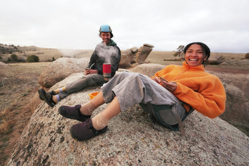 two people drinking coffee in the outdoors wearing deep plum leather suede mountain clogs