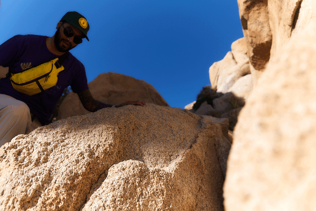 person scrambling up rocky granite wearing checkered socks and birch back leather suede mountain clogs