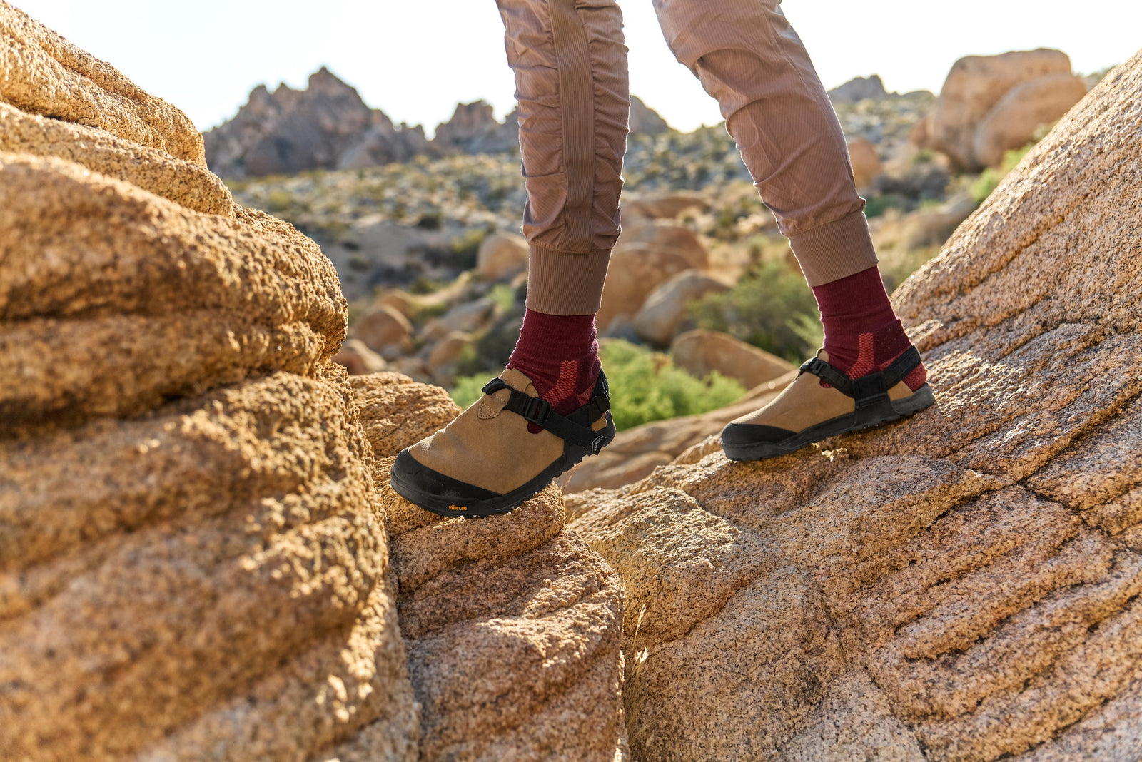 Person hiking on rocky terrain wearing birch bark leather suede mountain clogs and red socks.