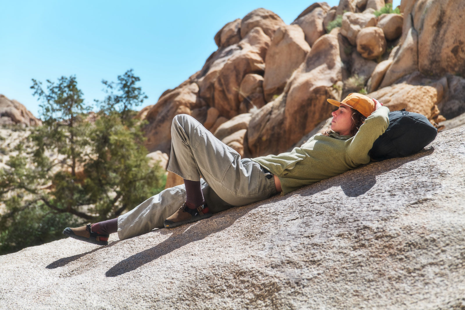 Person lying on a rock with a scenic background of trees and rocks wearing pinecone brown synthetic suede mountain clogs