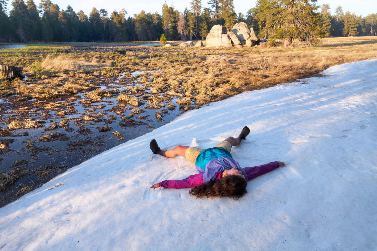 Person lying on a snowy surface wearing obsidian black synthetic suede clogs