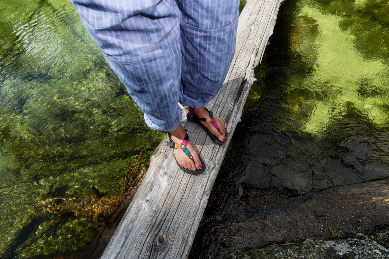 Person wearing Bedrock tourmaline cairn sandals standing on a log across water