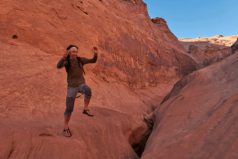 Person jumping between red clay colored sandstone rock slabs in the desert