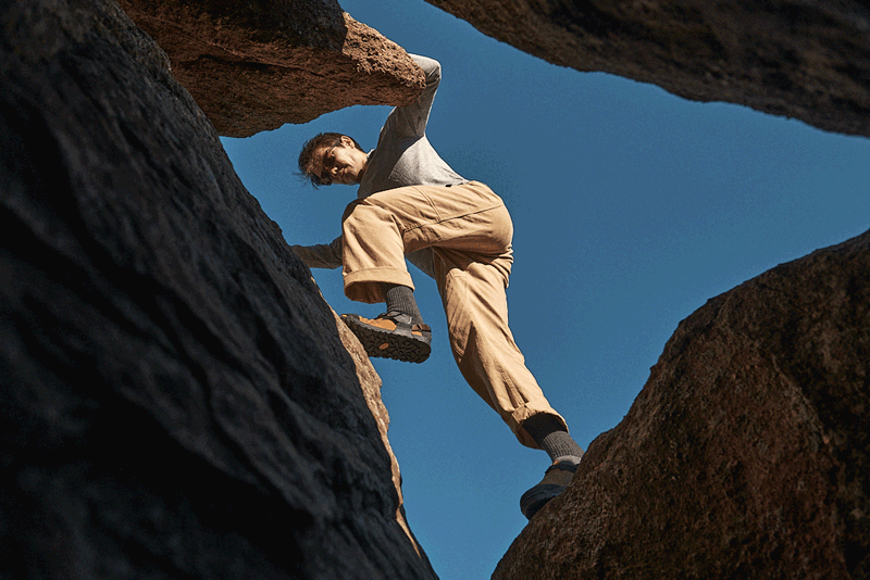 a person scrambling up a rock wearing brown nubuck leather mountain clogs