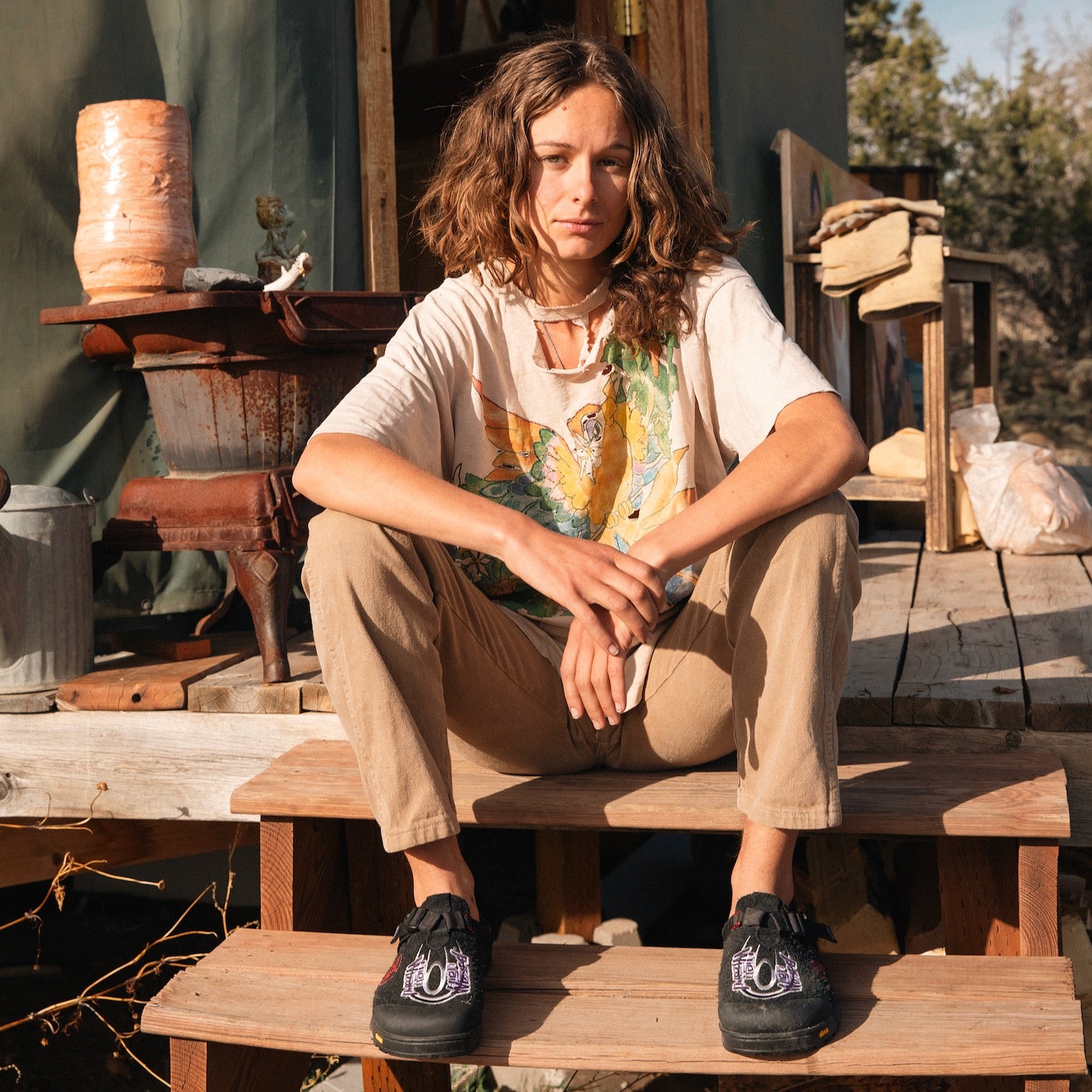 Person sitting on a wooden bench outdoors with rustic background wearing Stone Wizard phantom black clogs
