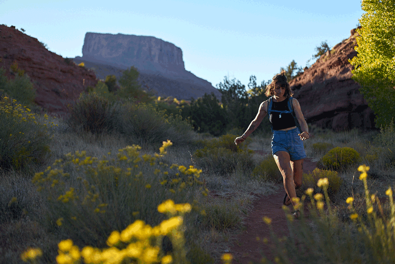 skipping along a trail in the deserst amidst flowers wearing cairn sandals