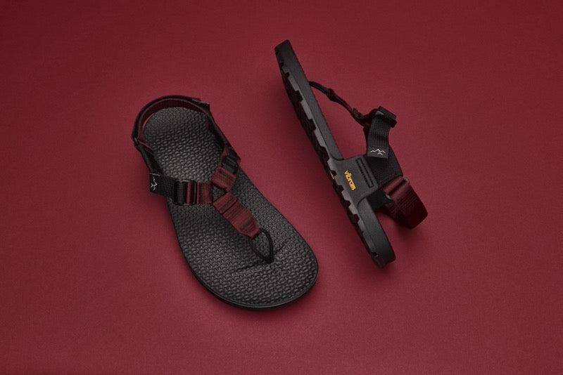 Studio photo of a pair of cairn evo 3d sandals with burgundy straps with a red backdrop.