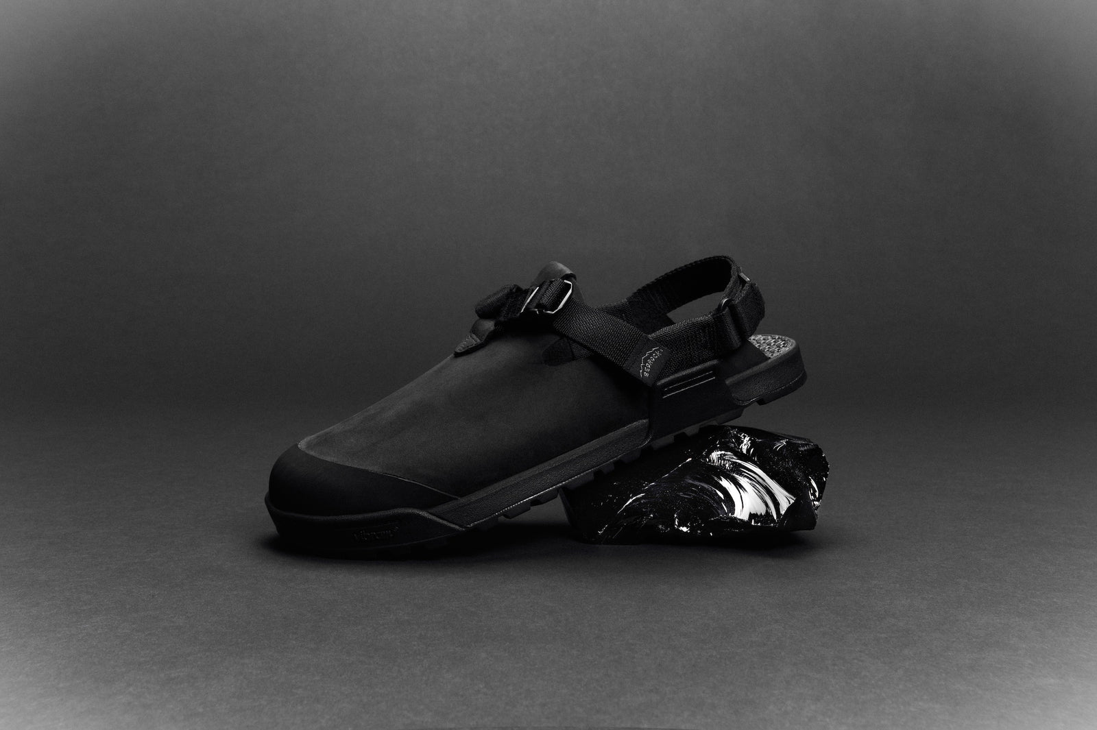 studio photo of Pobsidian dark gray nubuck leather mountain clog on a peice of volcanic rock