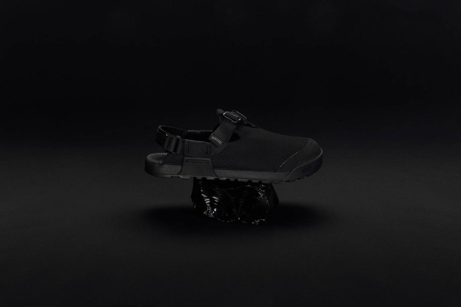 dark studio photo of obsidian black synthetic suede clogs sitting on a volcanic rock
