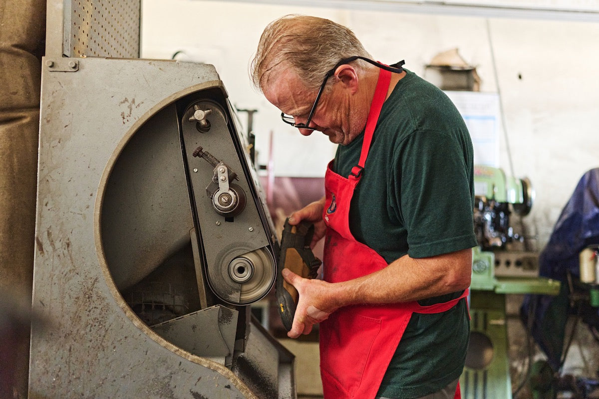 Person sanding down rubber outsole of a mountain clog in order to resoul 
