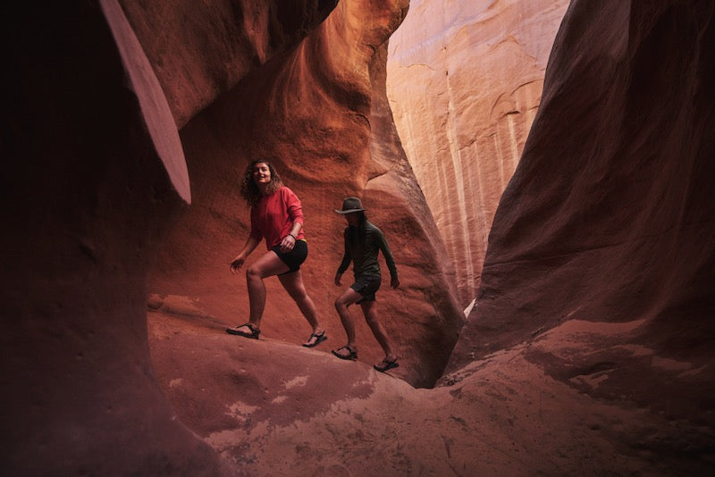two people hiking through a slot canyon in the desert wearing cairn evo sandals