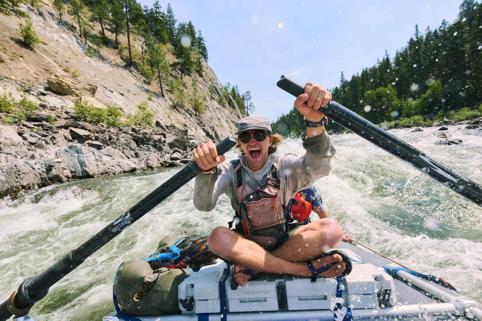 Man whitewater rafting sitting cross legged wearing Bedrock Cairn sandals