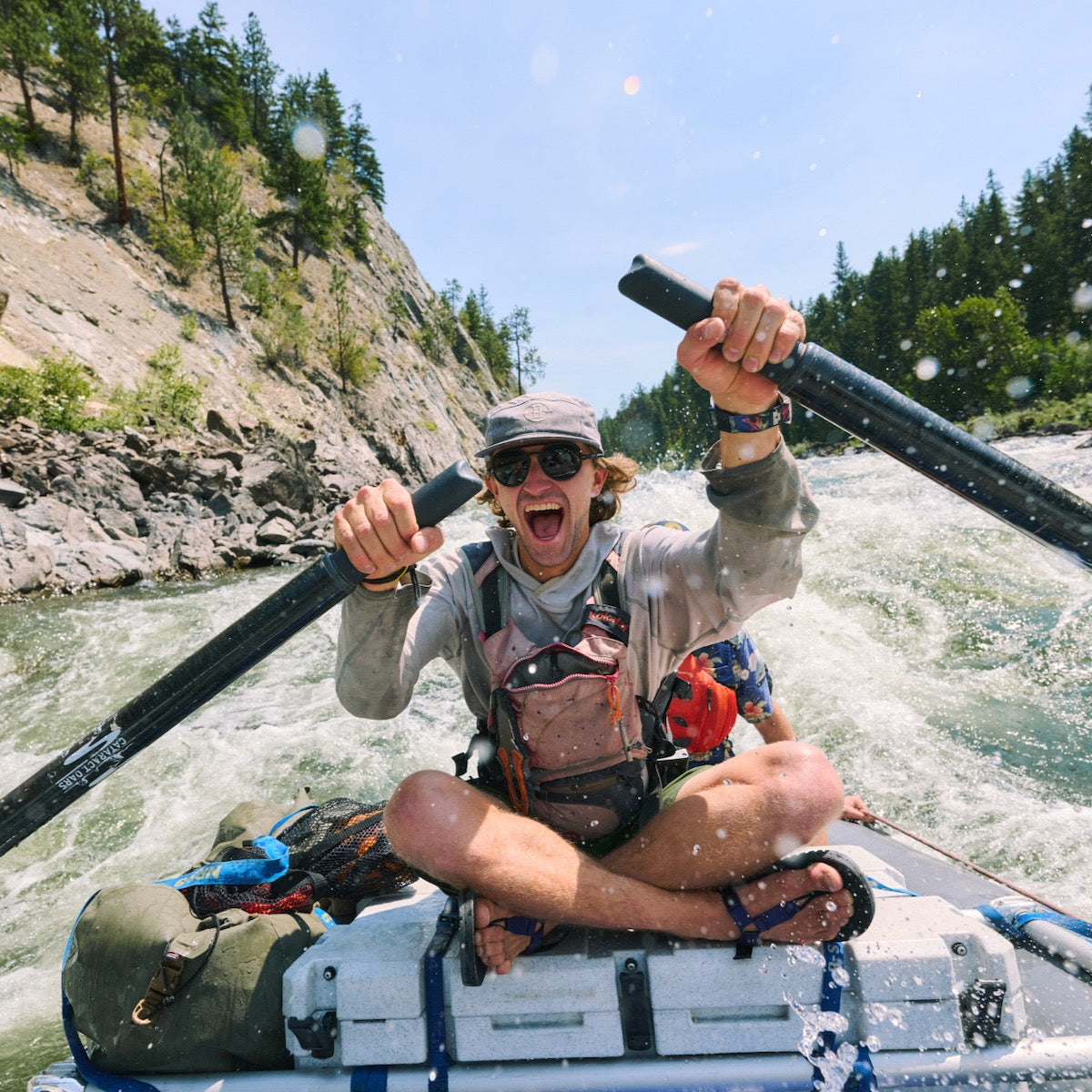 Man whitewater rafting sitting cross legged wearing Bedrock Cairn sandals