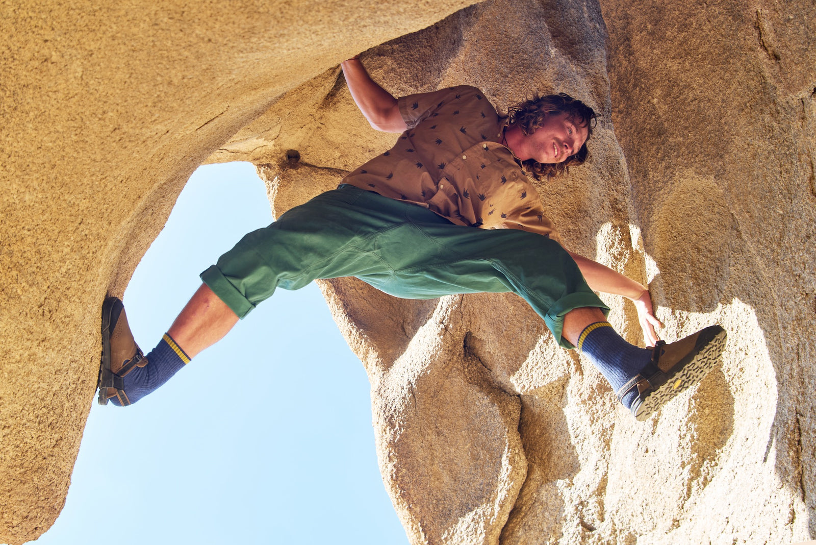 Person climbing a rock formation with a clear blue sky in the background and wearing pinecone brown synthetic suede mountain clogs 
