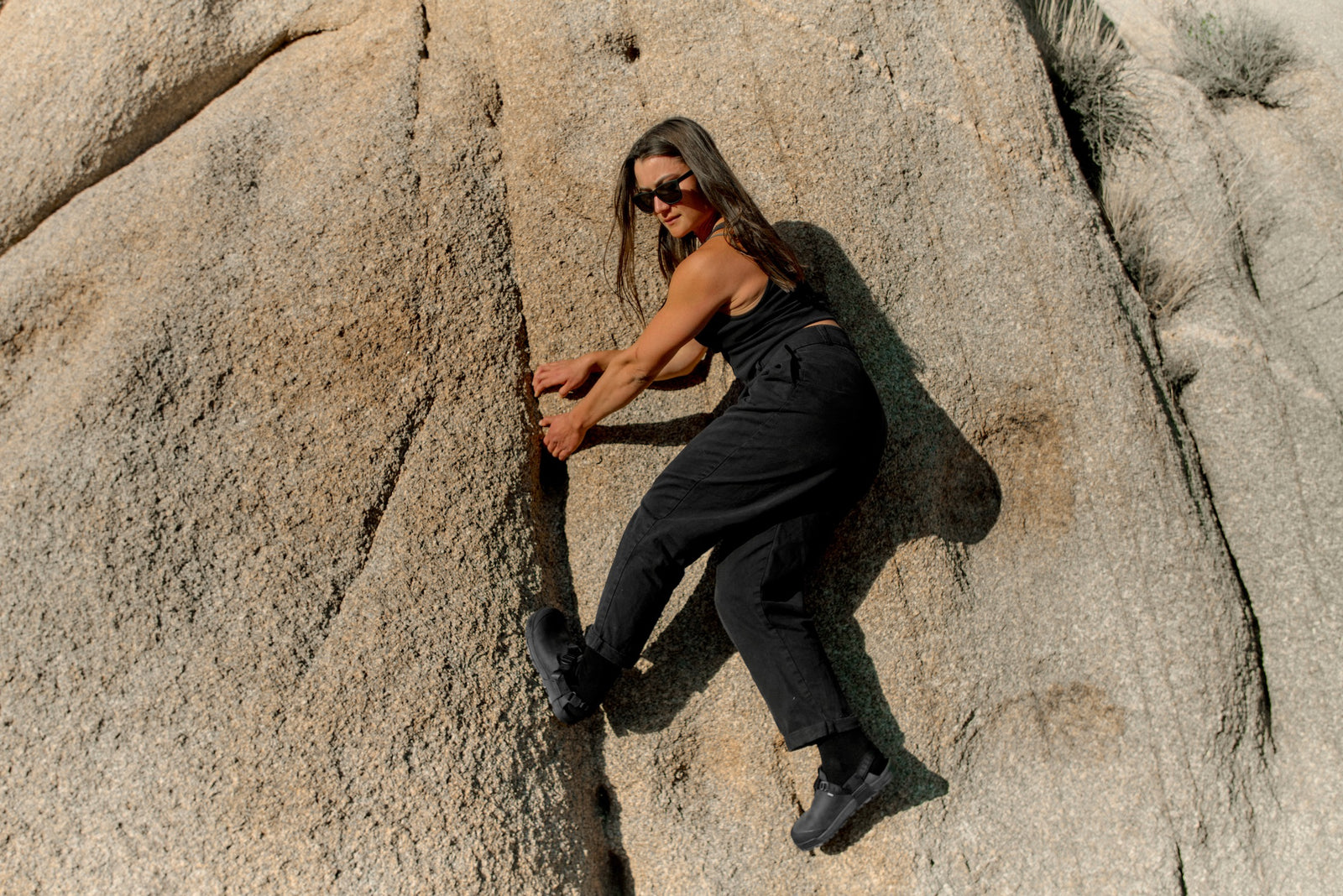 Person climbing a rocky cliff in a desert landscape wearing obsidian dark gray nubuck leather mountain clogs