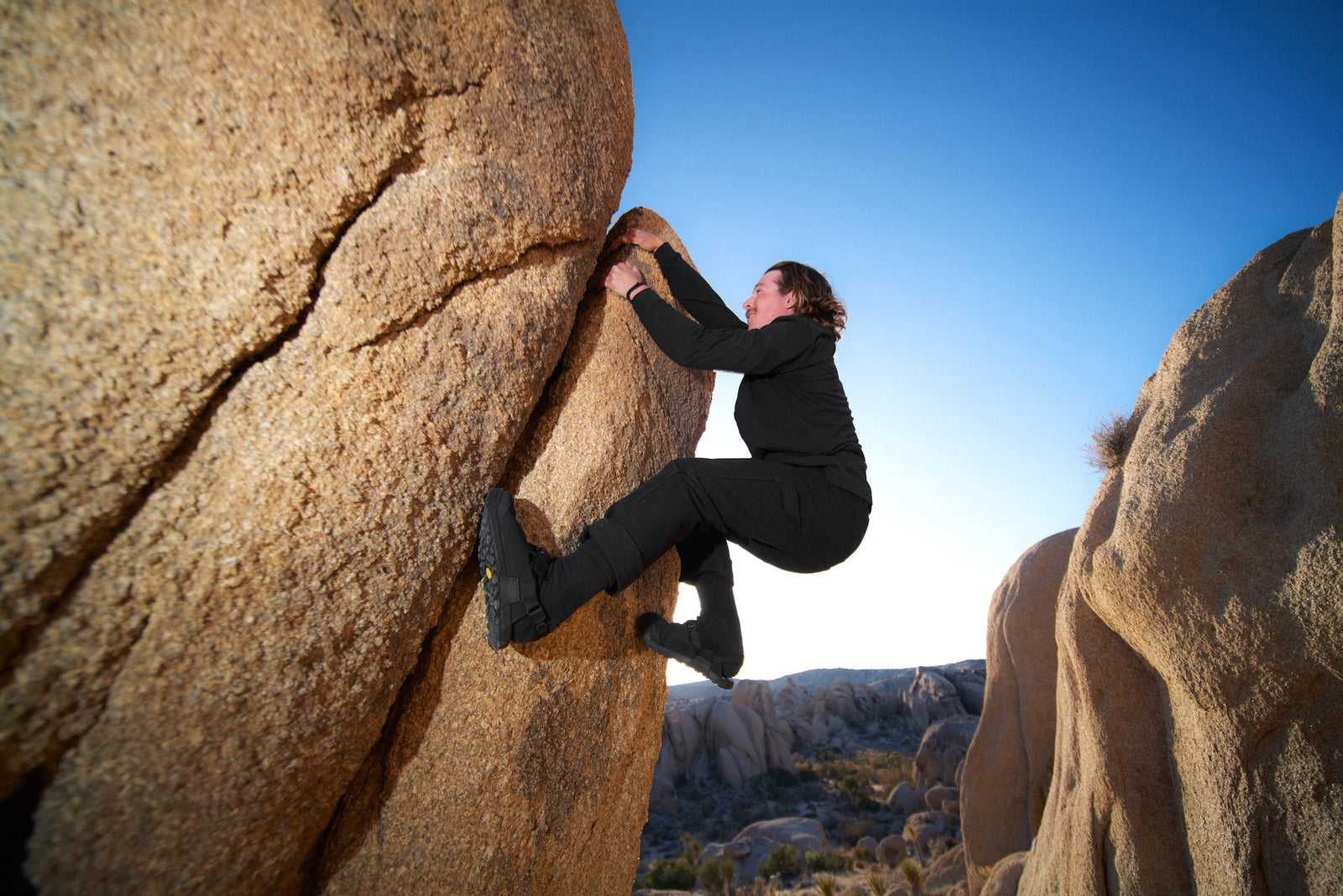 Person climbing a large rock formation in a desert landscape  wearing obsidian black synthetic suede clogs 