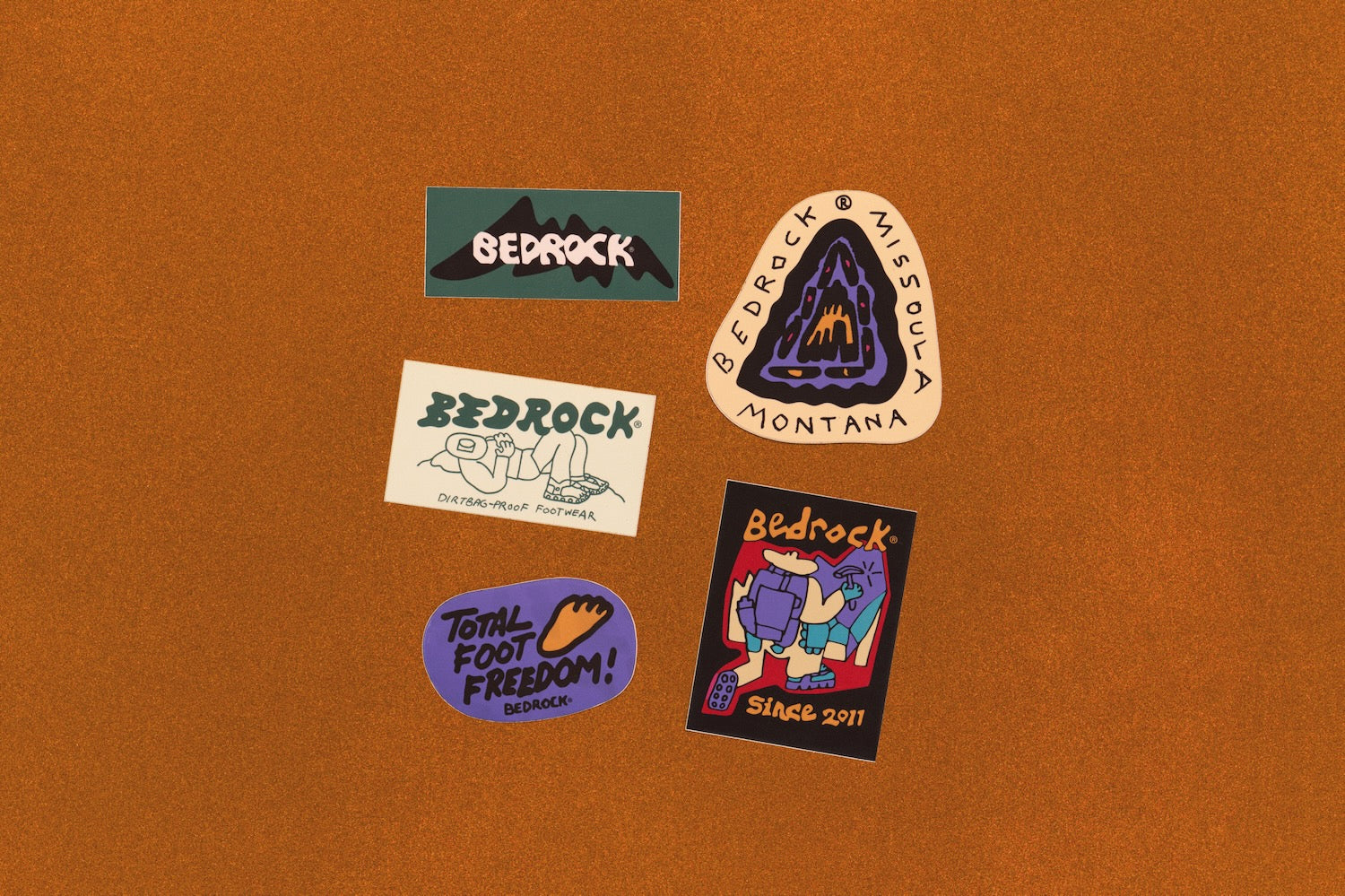 Five colorful Bedrock brand stickers arranged on a textured brown background.