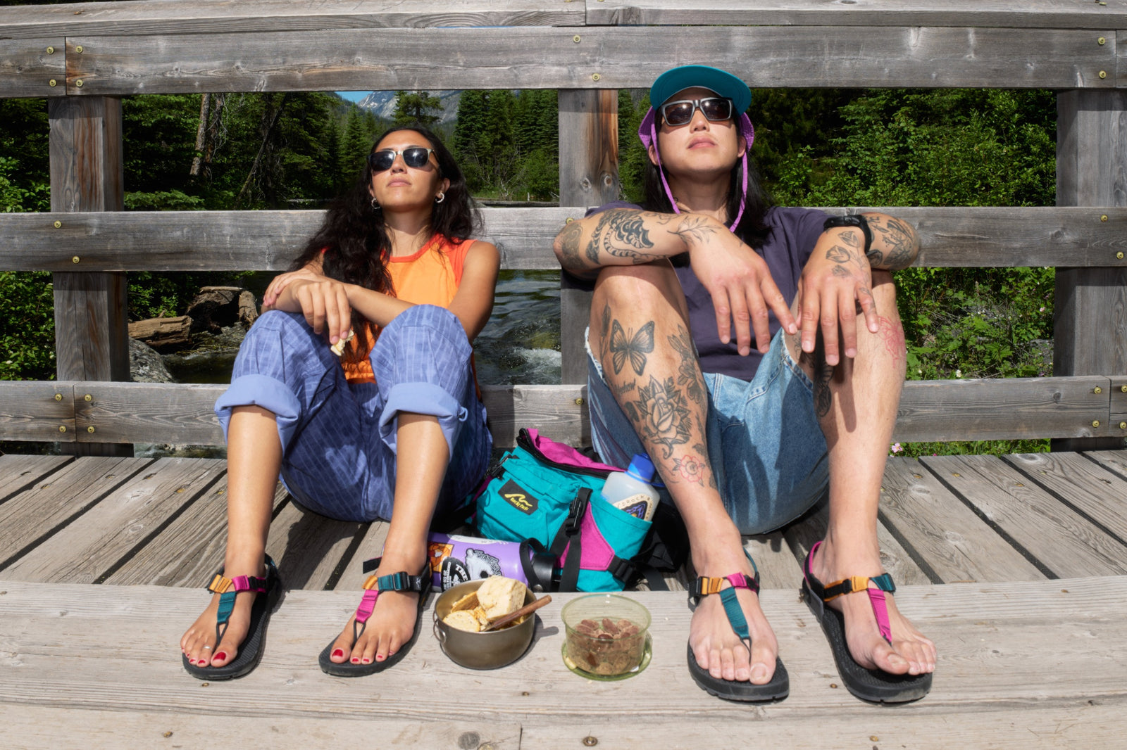 Two people eating snack sitting on a wooden bridge wearing Bedrock sandals