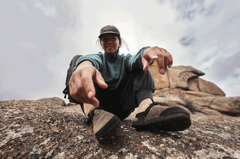 person sitting on rock smiling and wearing gray nubuck leather mountain clogs 