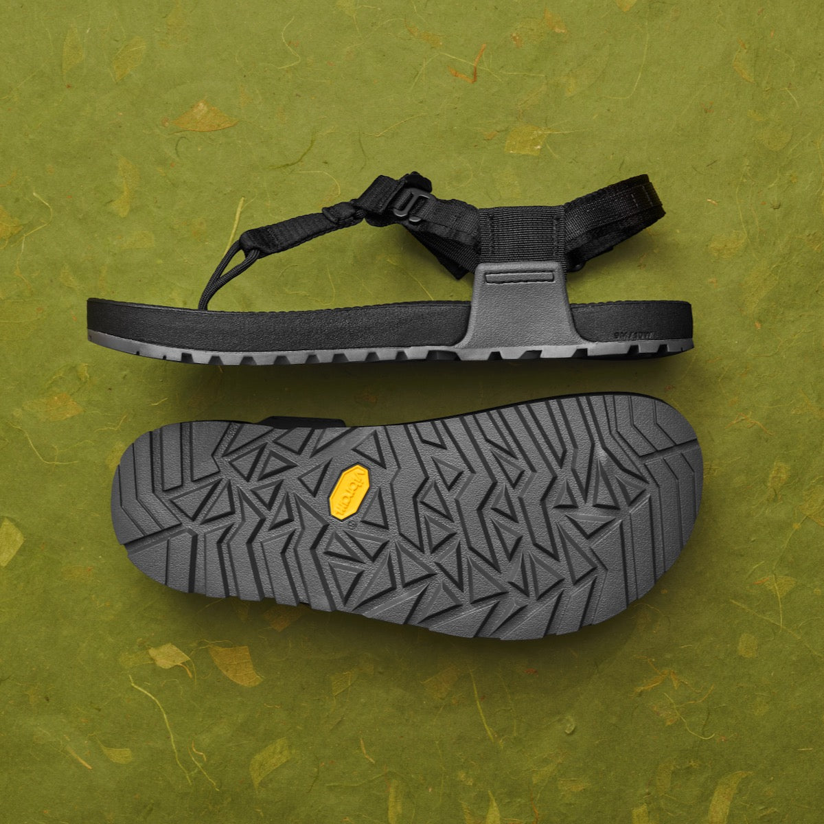 Black sandal with a textured sole on a green background