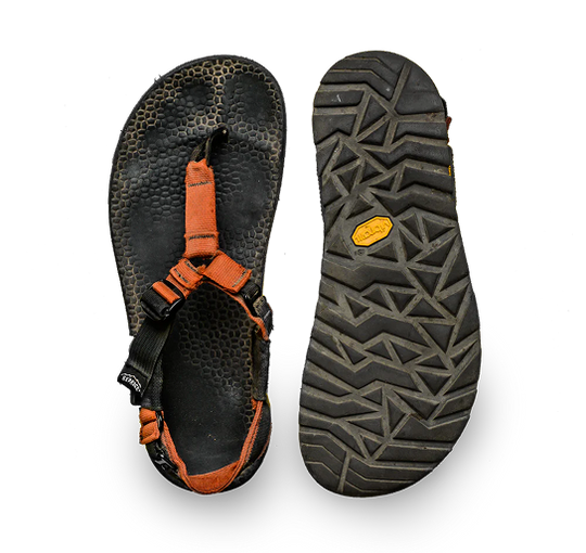 A pair of black and orange outdoor sandals shown from both the top and bottom views, highlighting the textured footbed and the aggressive tread pattern of the sole.